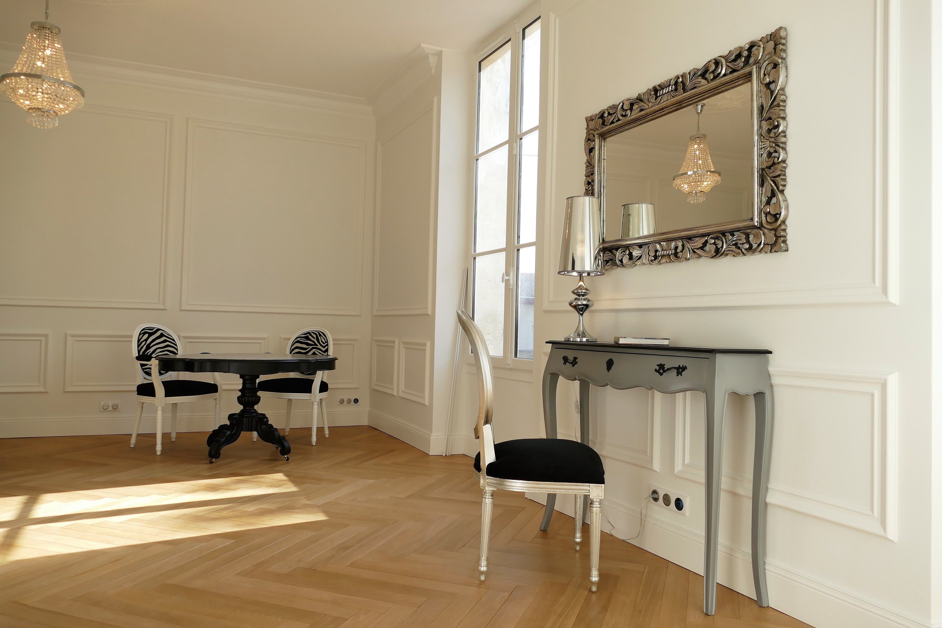Una habitación con una mesa de comedor, sillas, una consola con lámpara y un espejo grande y decorativo.