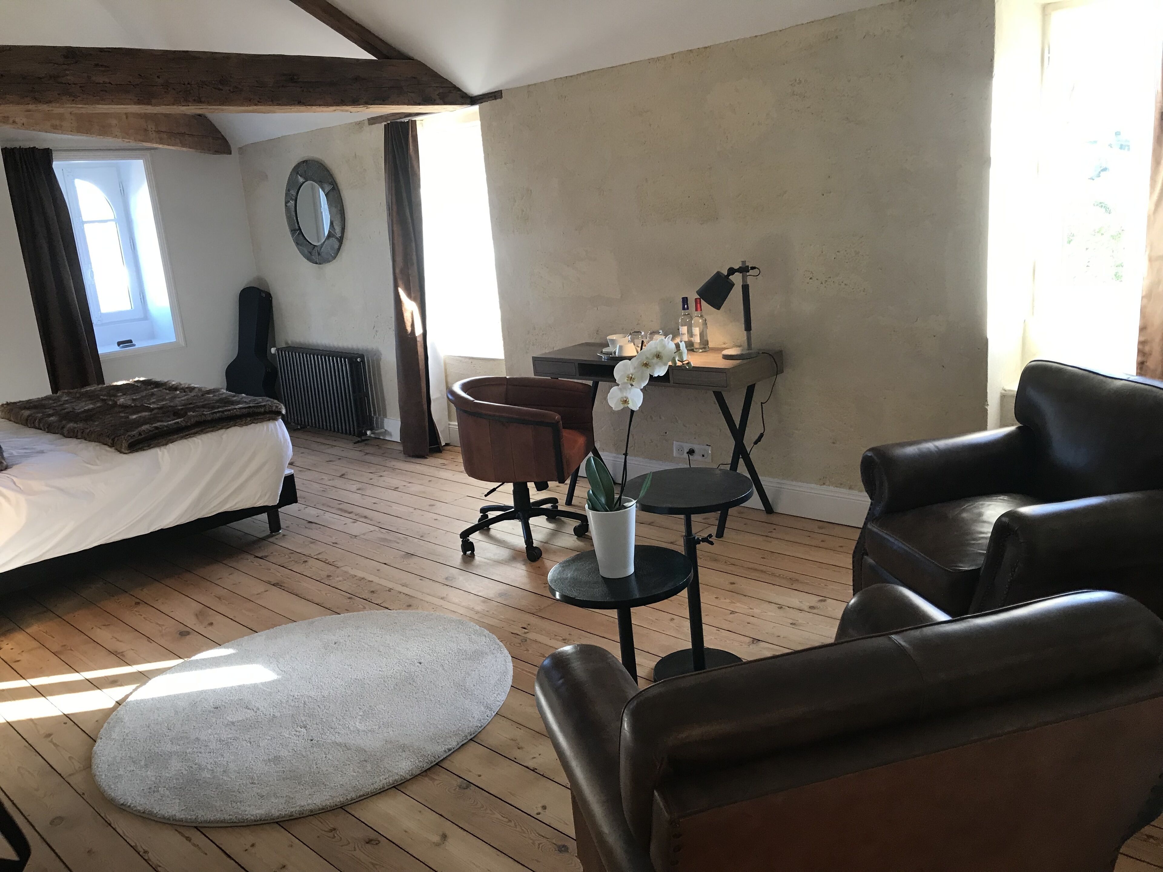A room with a bed, a desk, a chair, a round table, and a potted plant.