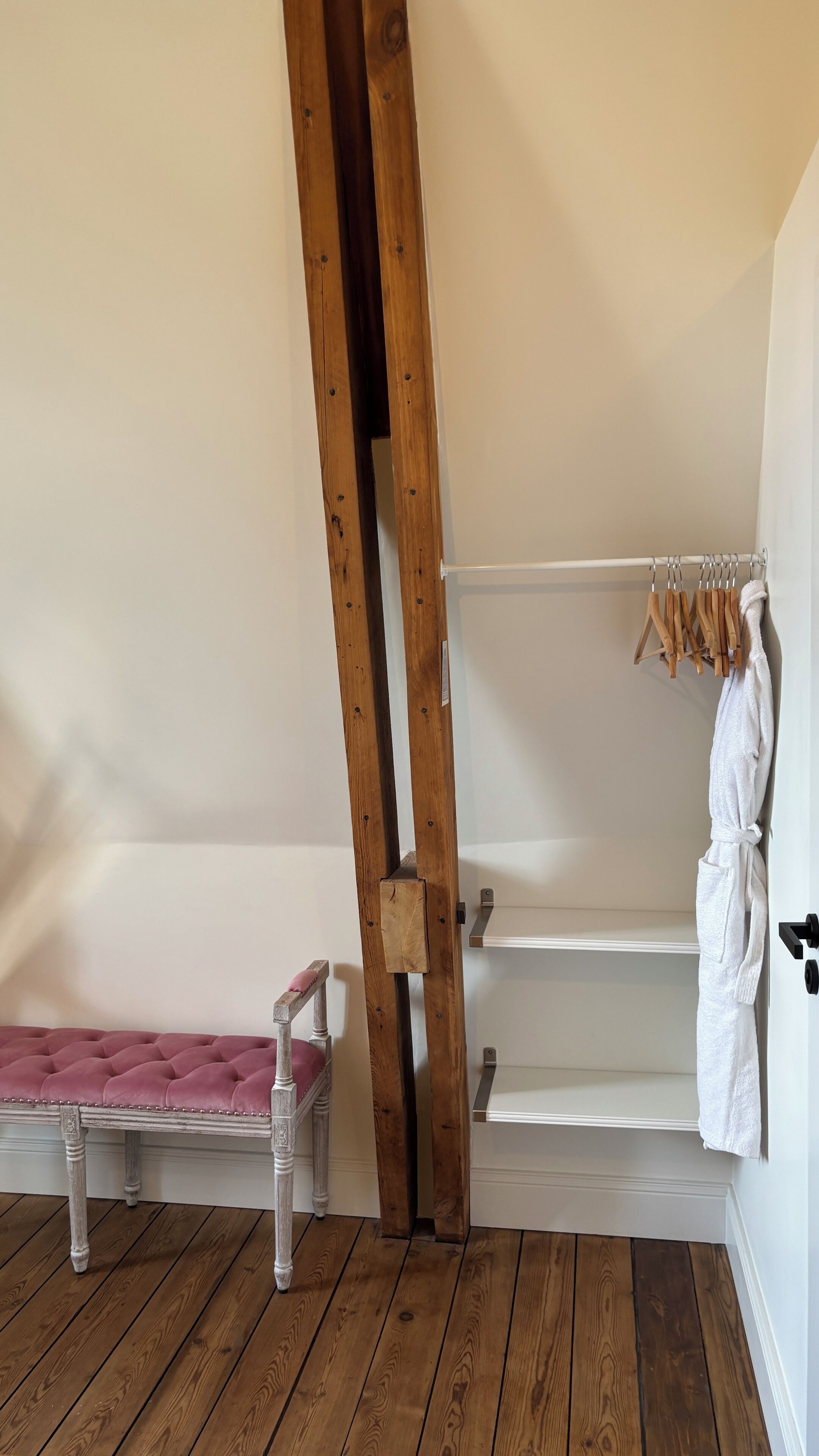 A room with a wooden bench, a white robe hanging on a rack, and a wooden ladder leaning against the wall.