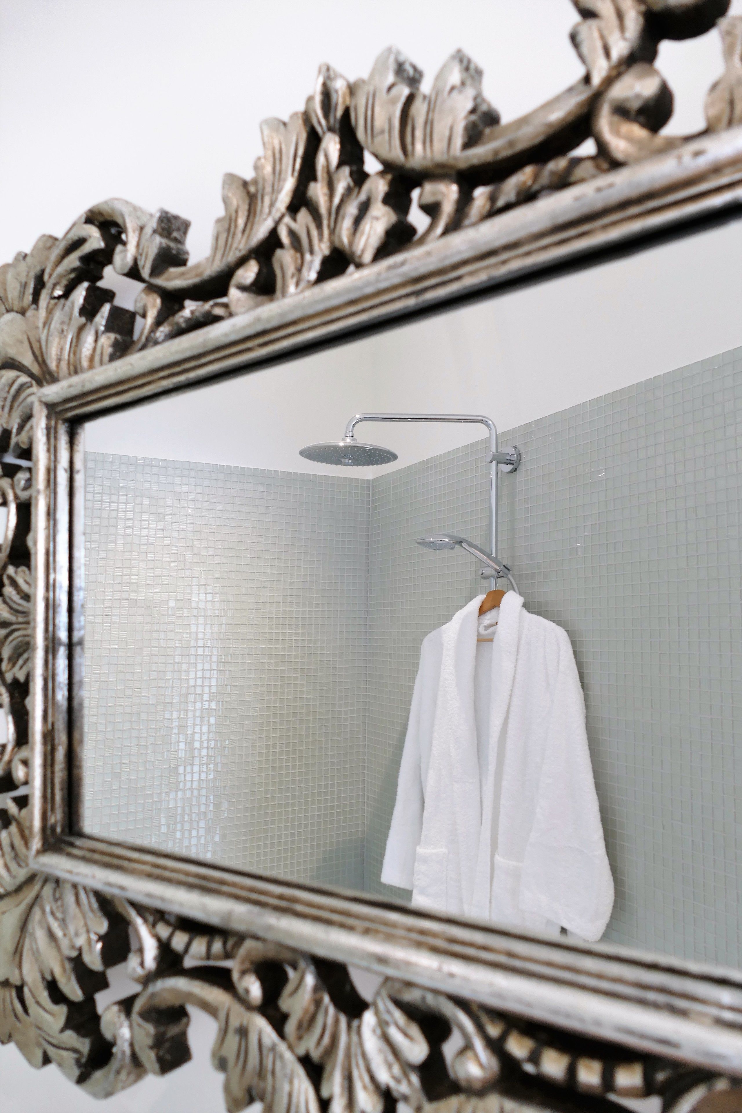 Een badkamer met een douche, een spiegel met een versierde lijst, en een witte handdoek aan een rek.