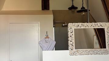 A bedroom with a white door, a hanging robe, a mirror with an ornate frame, and a bed with a pink blanket.