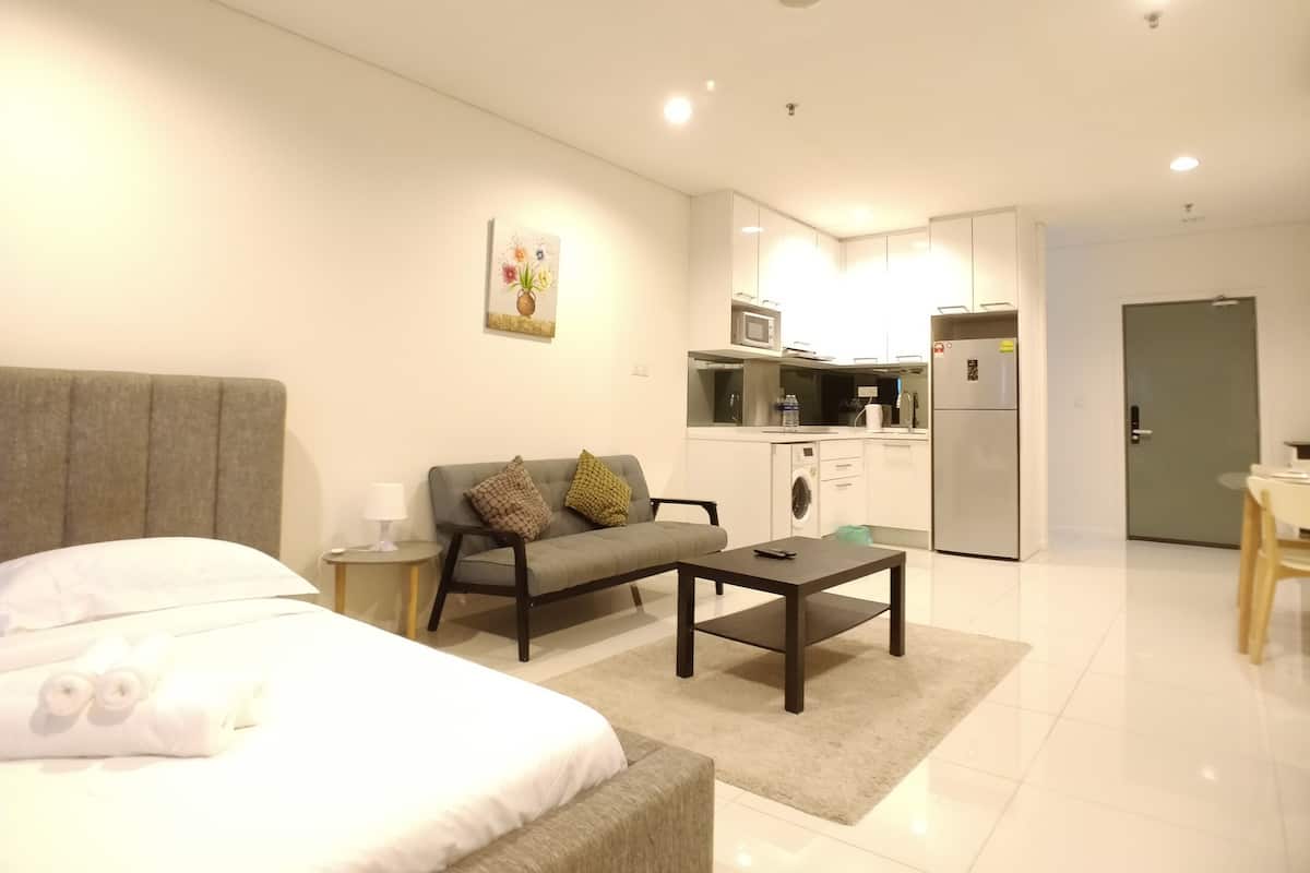 Une chambre d’hôtel moderne avec un lit, un canapé, une table basse et, au fond, une kitchenette.