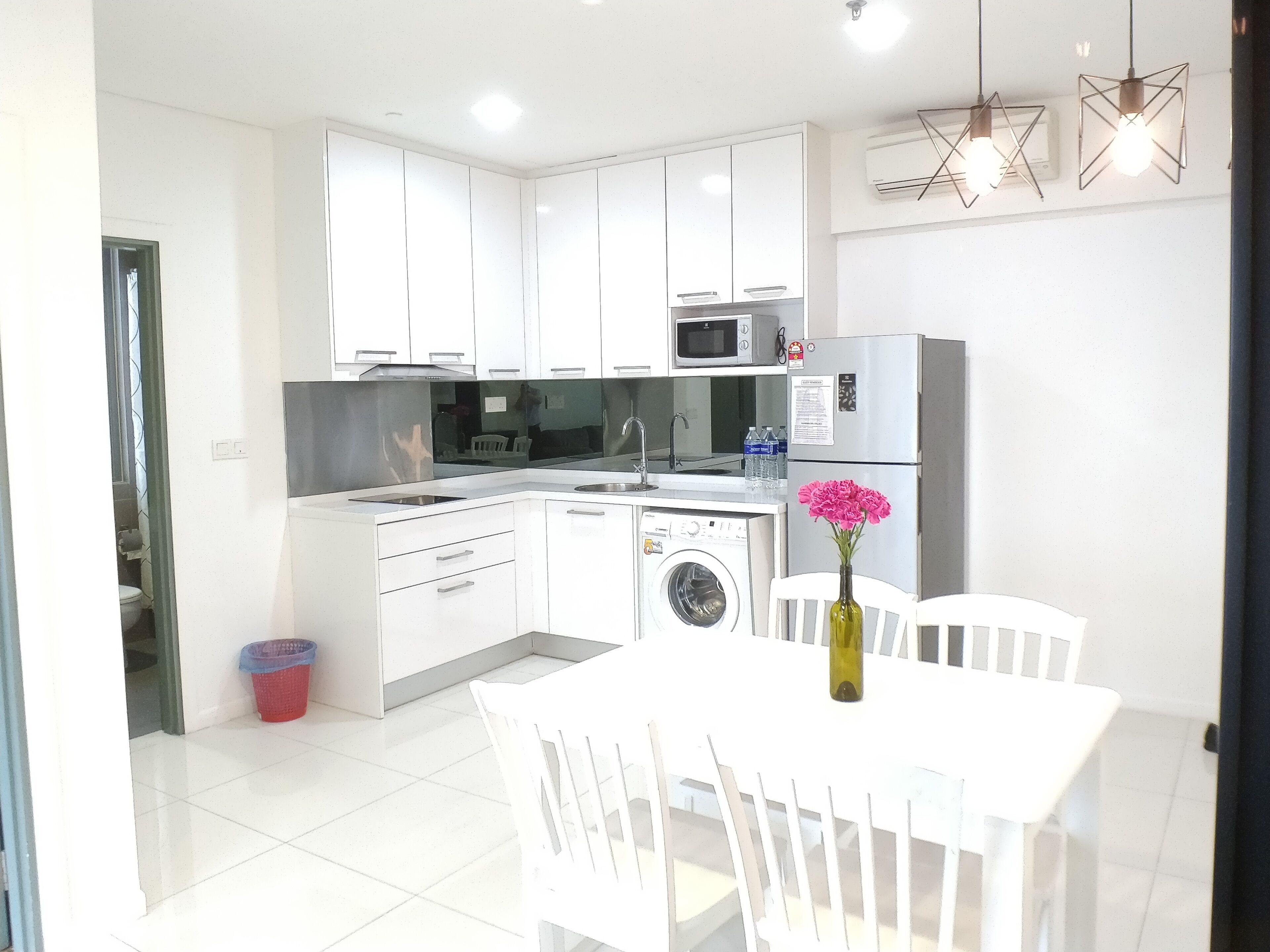 A modern kitchen with white cabinets, a microwave, a refrigerator, a washing machine, and a dining area with a table and chairs.