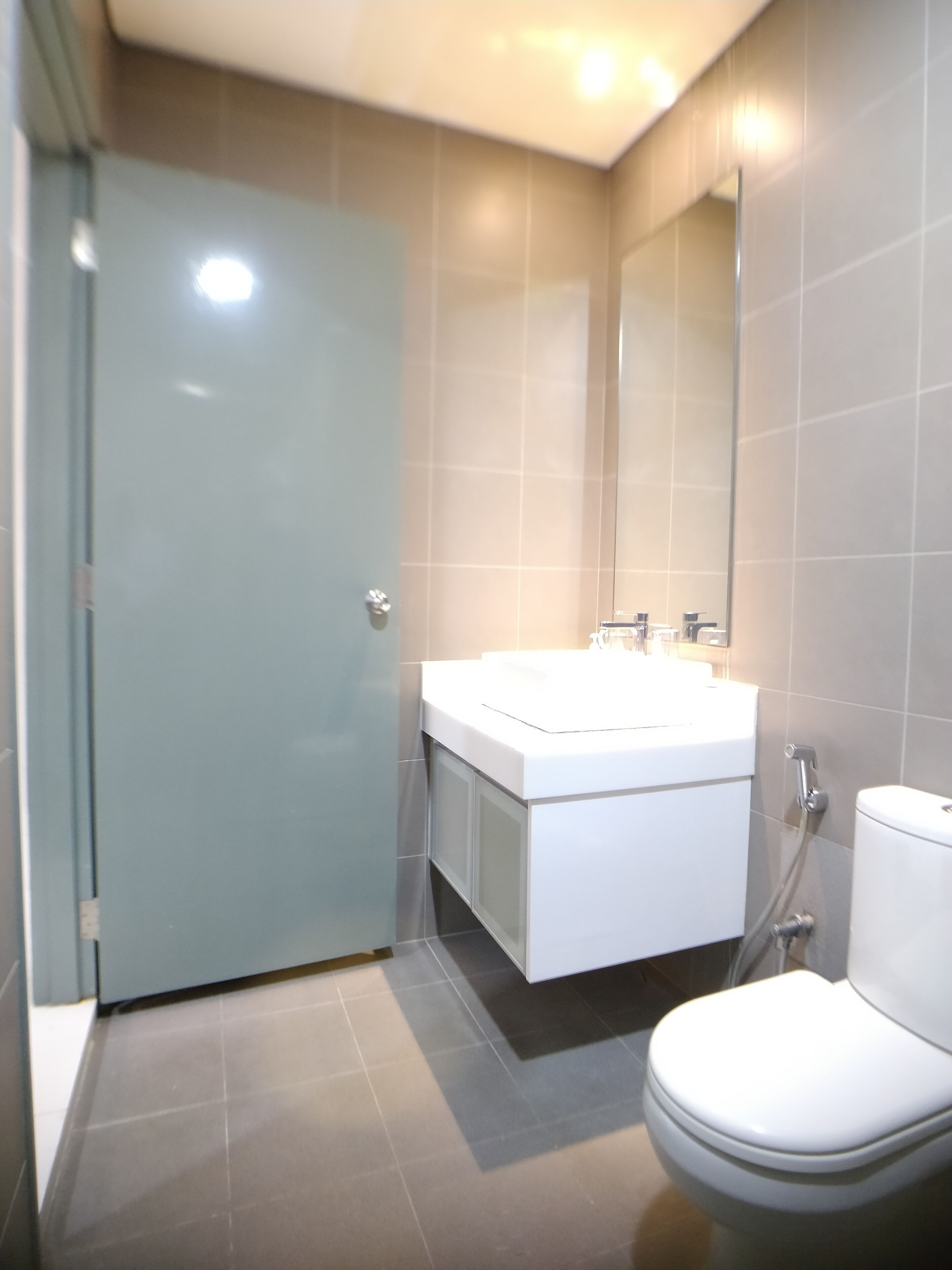 Un baño moderno con puerta de vidrio, lavamanos blanco y un inodoro.