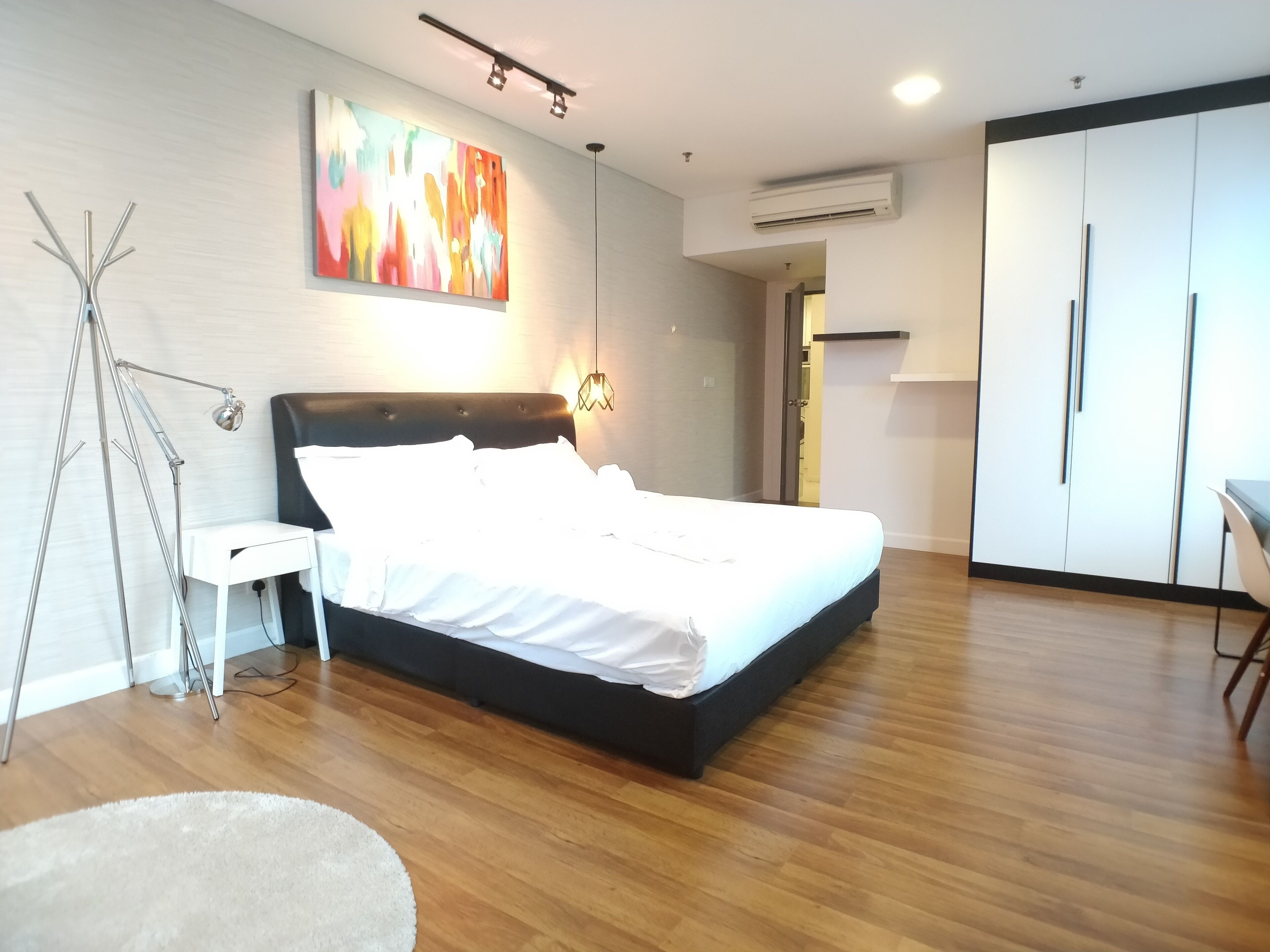 A modern bedroom with a bed, a bedside lamp, a floor lamp, a painting, and a wardrobe.