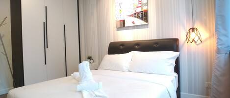 A neatly made bed with white linens and a folded towel, a black headboard, and a wall-mounted light fixture.