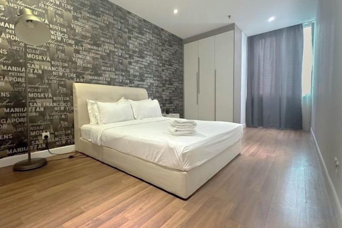 Quarto com uma cama grande, parede com nomes de cidades e piso de madeira.