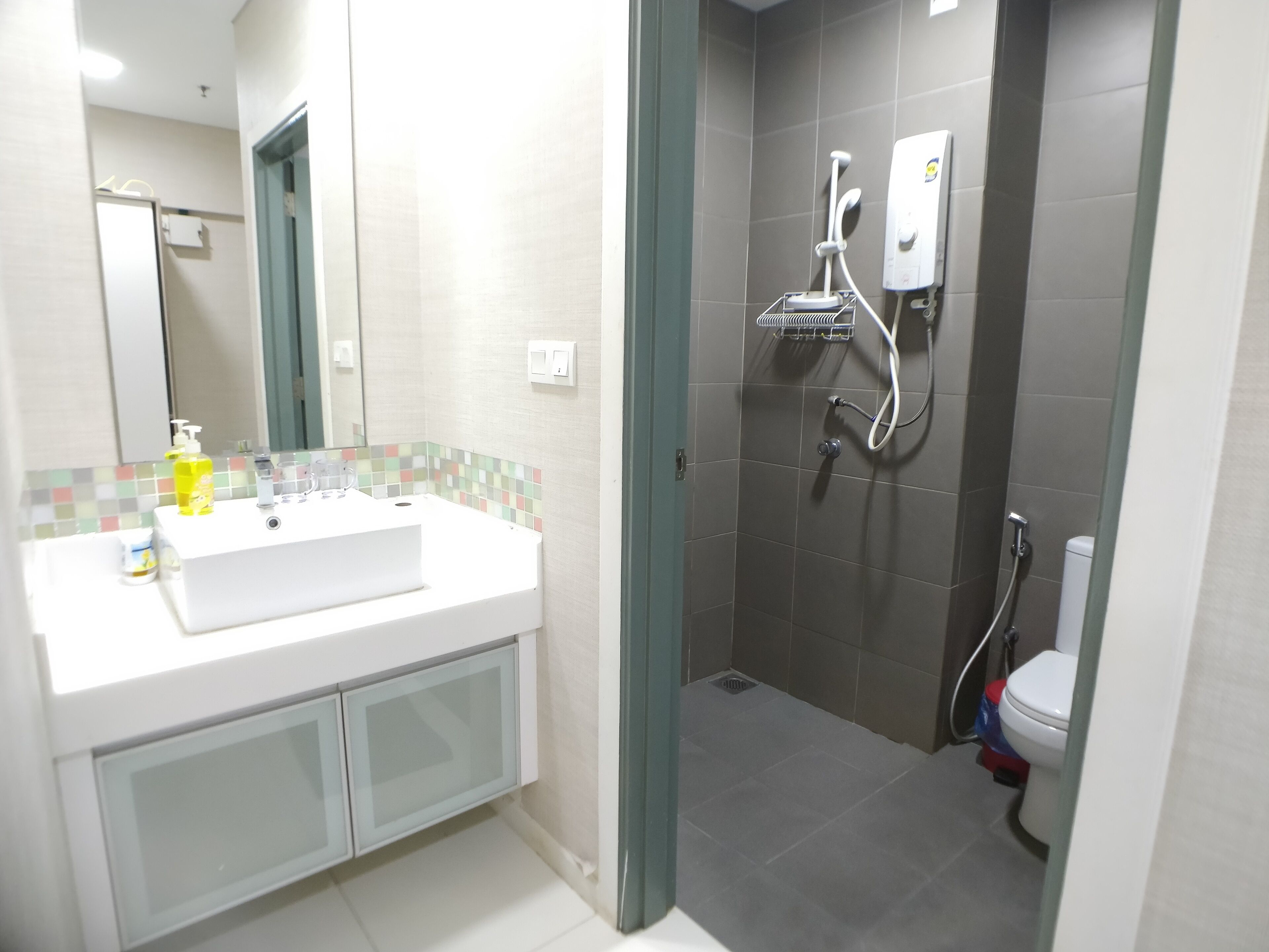 A modern bathroom with a white sink, a glass cabinet, a shower with a handheld showerhead, and a toilet.