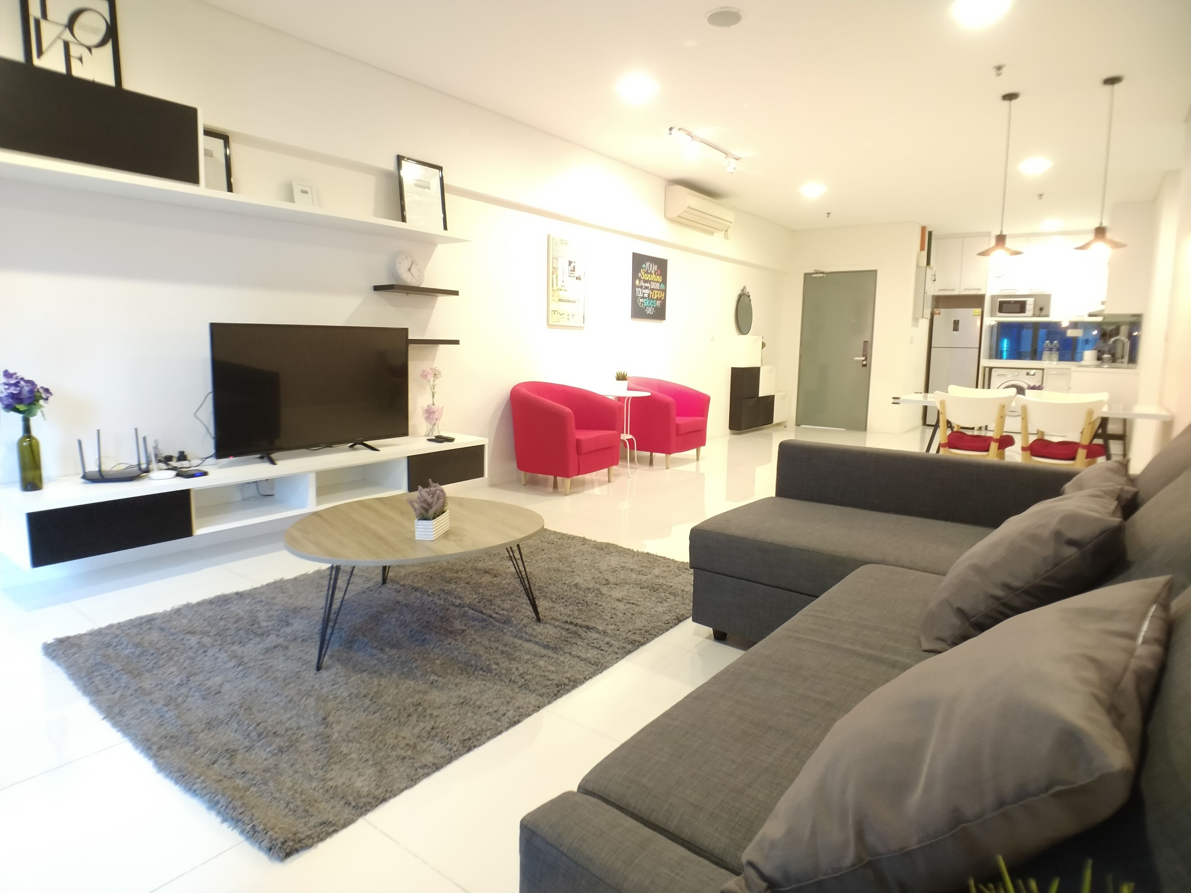 A modern living room with a grey sofa, a flat-screen TV, a coffee table, and red chairs.