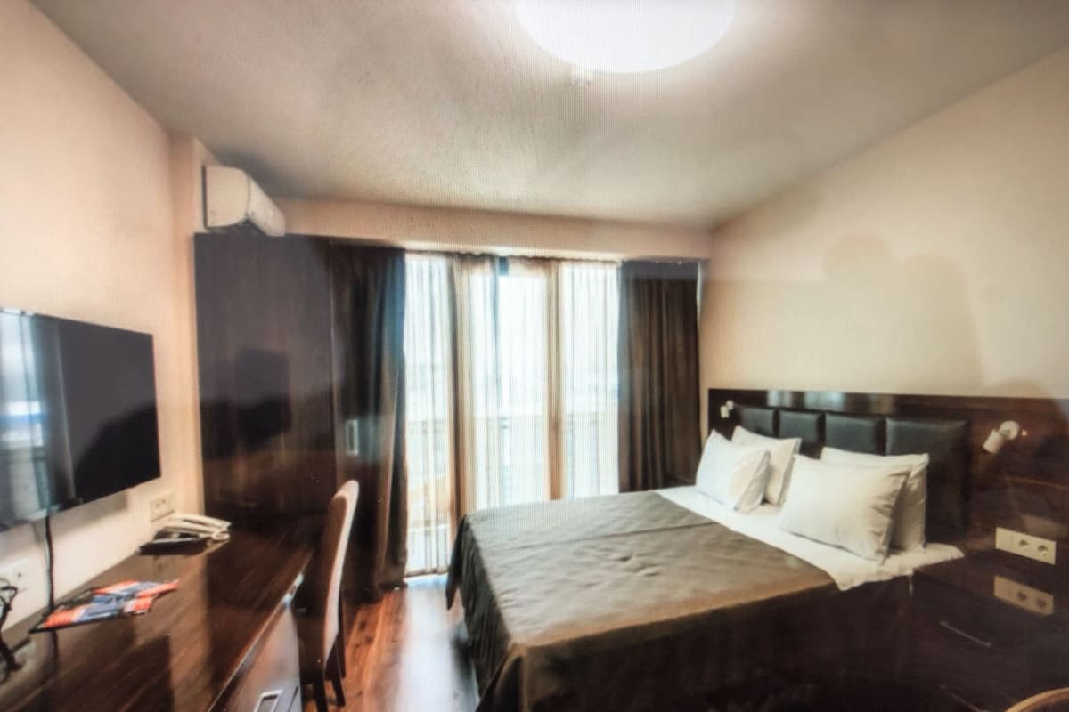 A hotel room with a bed, a desk, a chair, a TV, and a window with curtains.