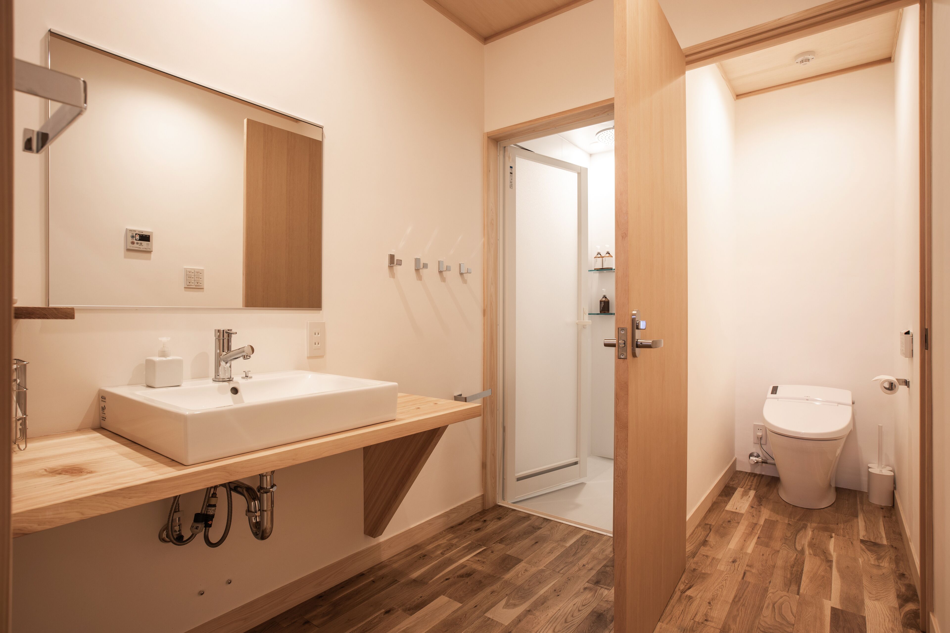 A modern bathroom with a wooden vanity, a large mirror, a toilet, and a shower area.