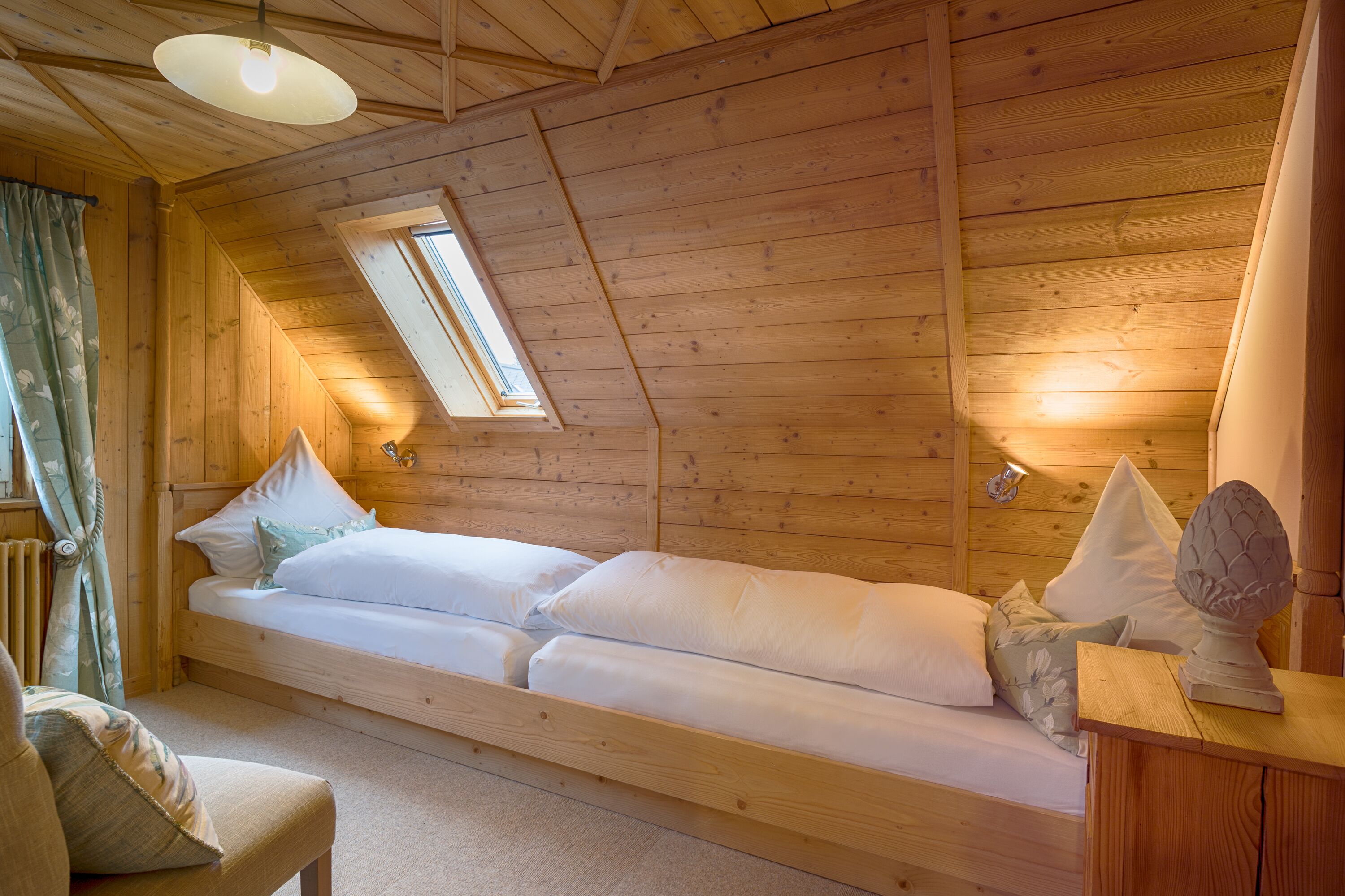 Ein Holzhütten-Zimmer mit Schlafkoje, kleinem Tisch und einem fenster mit Vorhängen.