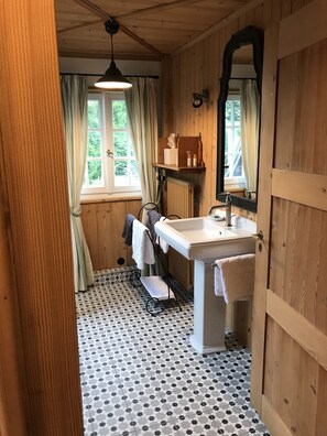 Casa de banho com lavatório branco, espelho e janela com cortinas.