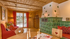 A cozy room with wooden walls and ceiling, a green fireplace, a dining table with candles, and red patterned furniture. - Chalet am Birkenhain (Hinterzarten)