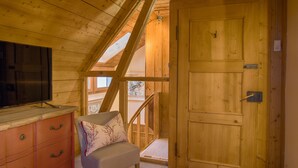 A wooden interior with a television on a dresser, a chair with a cushion, and a wooden door. - Chalet am Birkenhain (Hinterzarten)