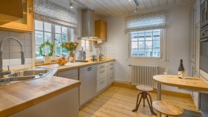 A modern kitchen with wooden cabinets, a built-in dishwasher, a window with a view, and a small dining table with chairs. - Chalet am Birkenhain (Hinterzarten)