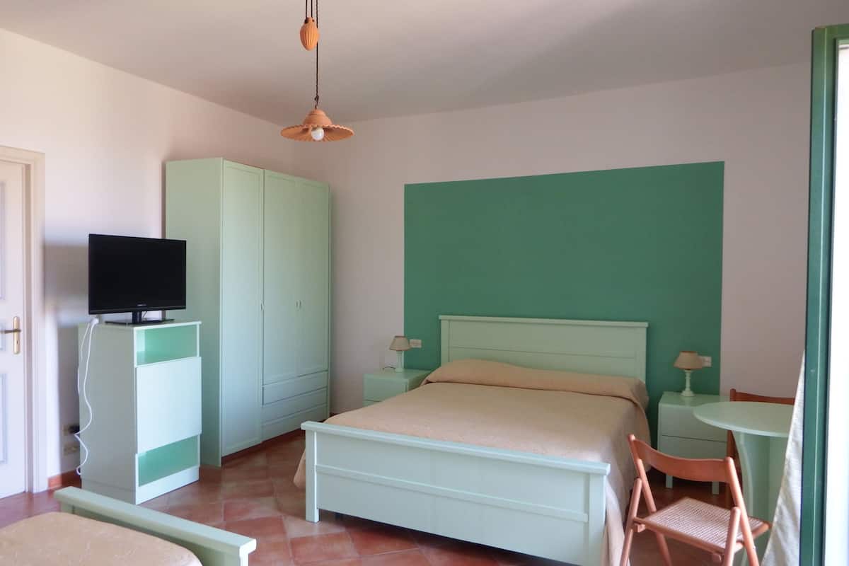 A bedroom with a bed, a television on a cabinet, a chair, a table, and a lamp.