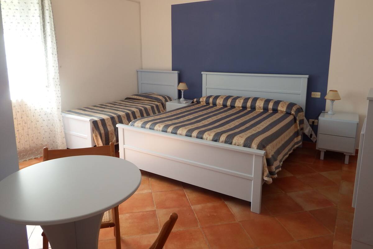 A bedroom with two beds, a small table, and a chair.