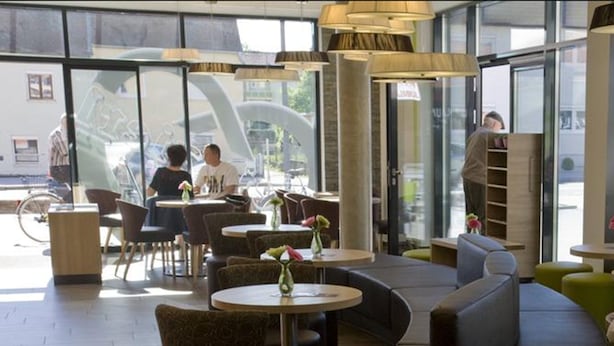 Ein modernes Café mit runden Tischen, gepolsterten Sitzplätzen und großen Fenstern.