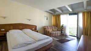 Ein Hotelzimmer mit einem großen Bett, einem Sessel, einem kleinen Tisch mit Pflanze und einem Balkon mit Vorhängen.