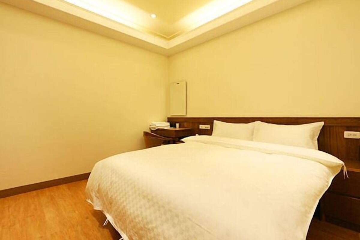 A hotel room with a large bed, a nightstand, and a mirror on the wall.