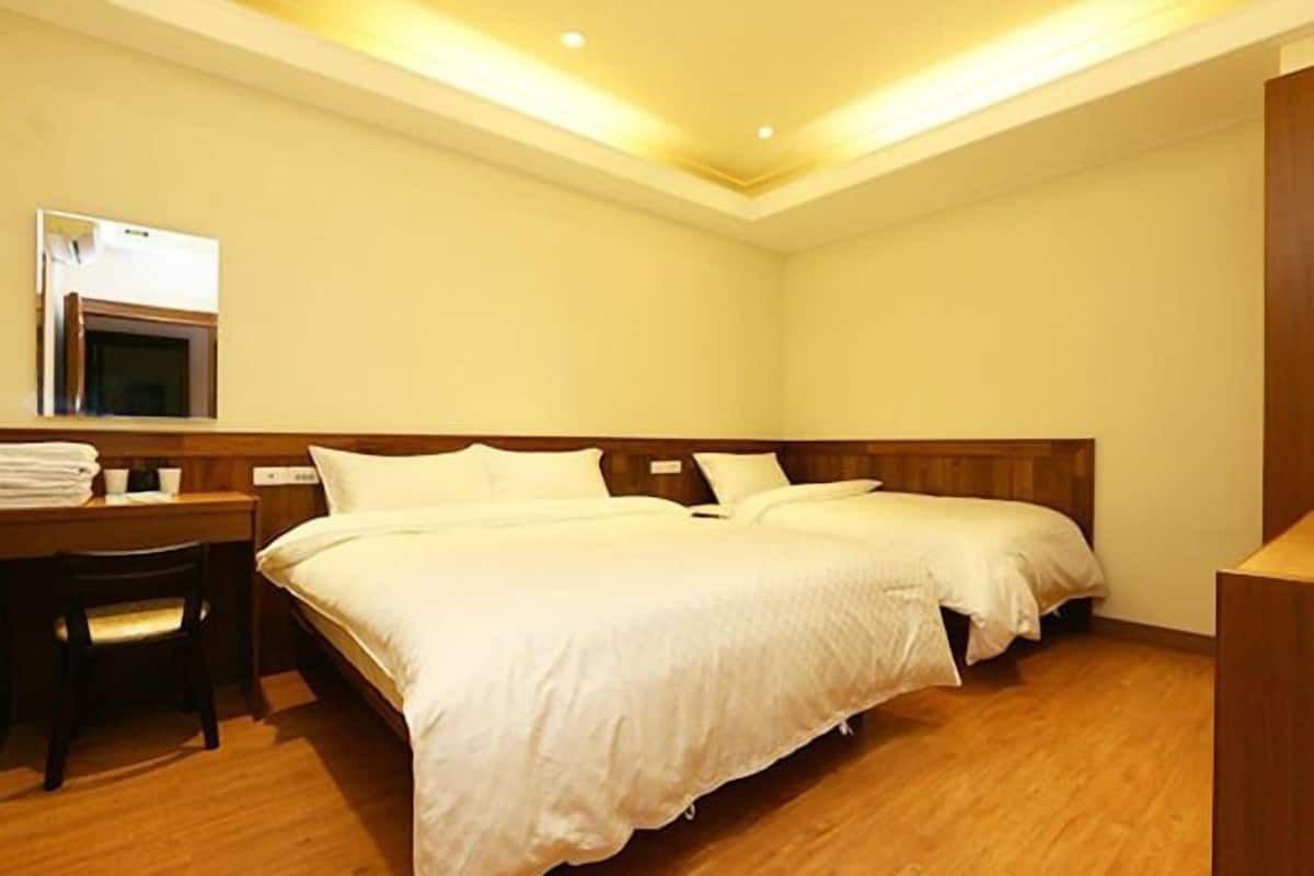 A hotel room with two beds, a desk with a chair, and a microwave on the wall.