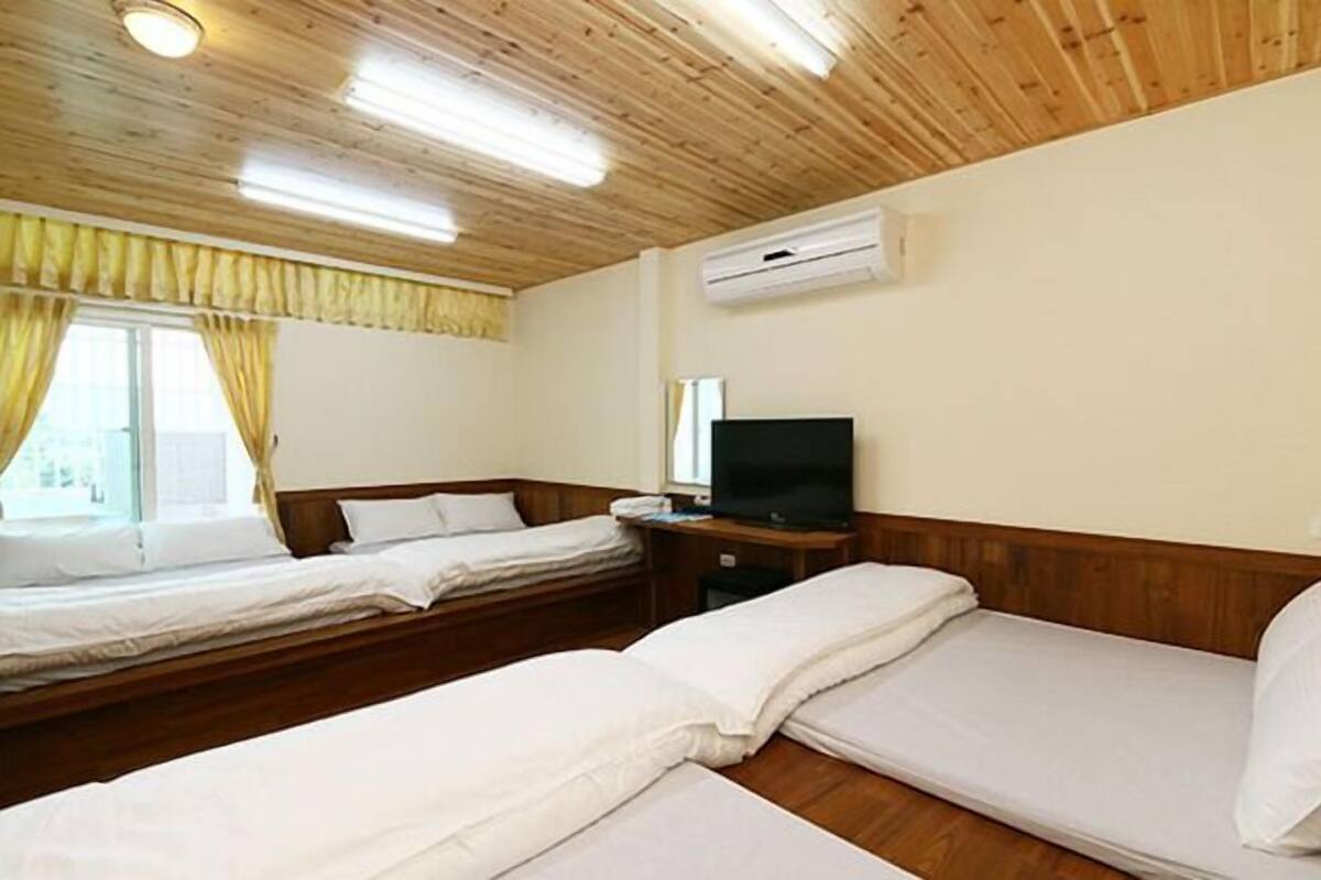 A hotel room with two beds, a television, and an air conditioning unit.