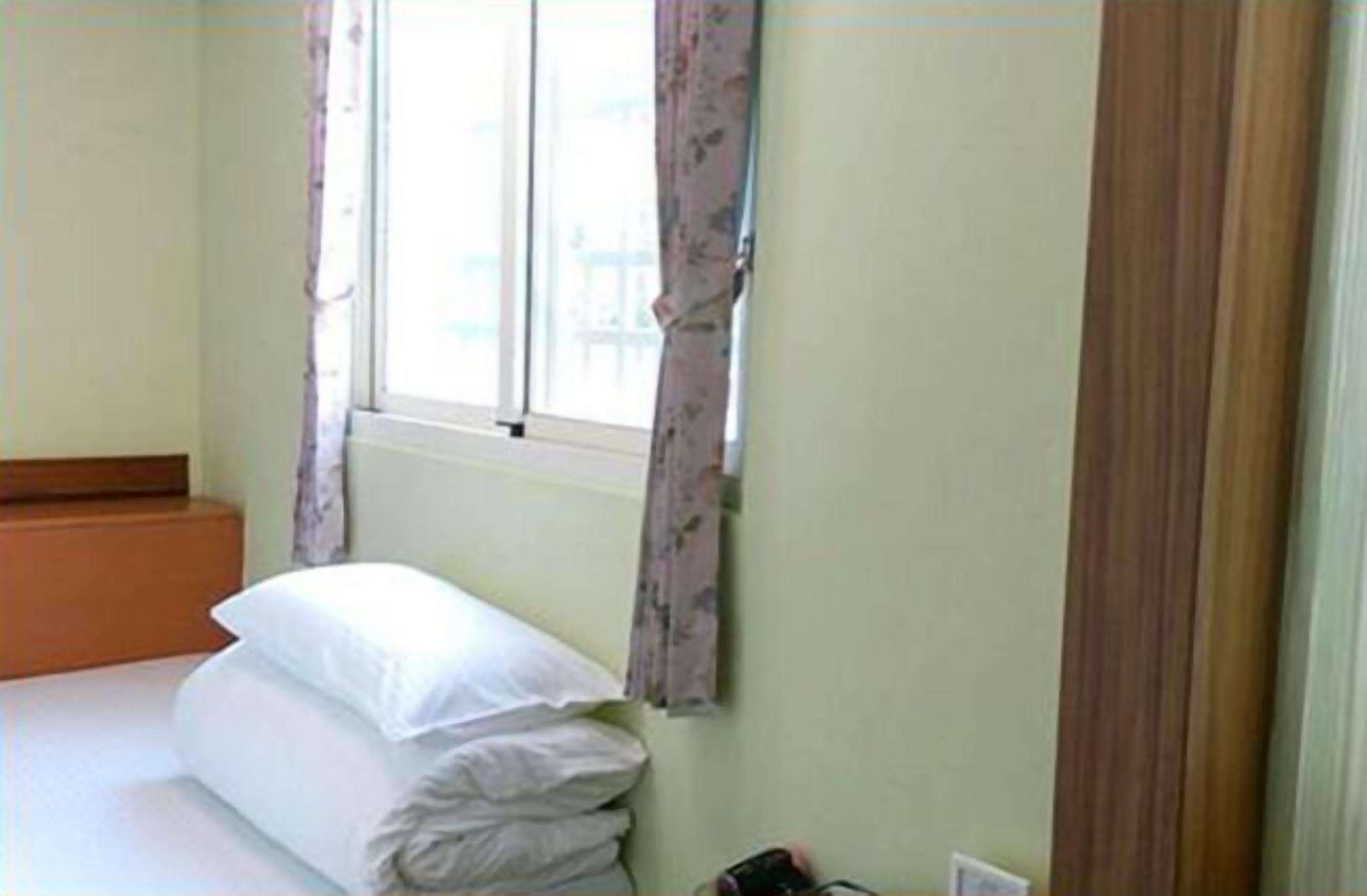 A small, neatly made bed with white linens in a room with light green walls.