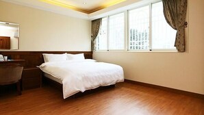 A hotel room with a wooden floor, a large bed, a bedside table, a chair, and a window with curtains. - Happy Owner Homestay (Ruisui)