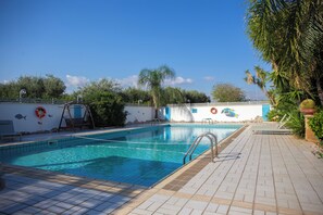 A swimming pool with a tiled deck, surrounded by palm trees and a decorative wall with fish motifs.