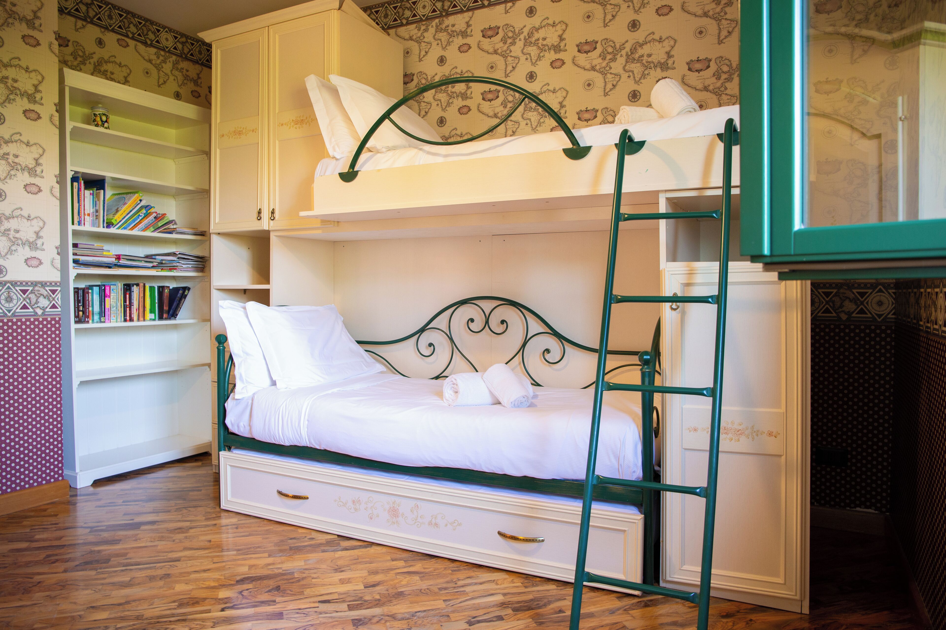 Una cama litera con escalera, una estantería y un papel tapiz estampado.