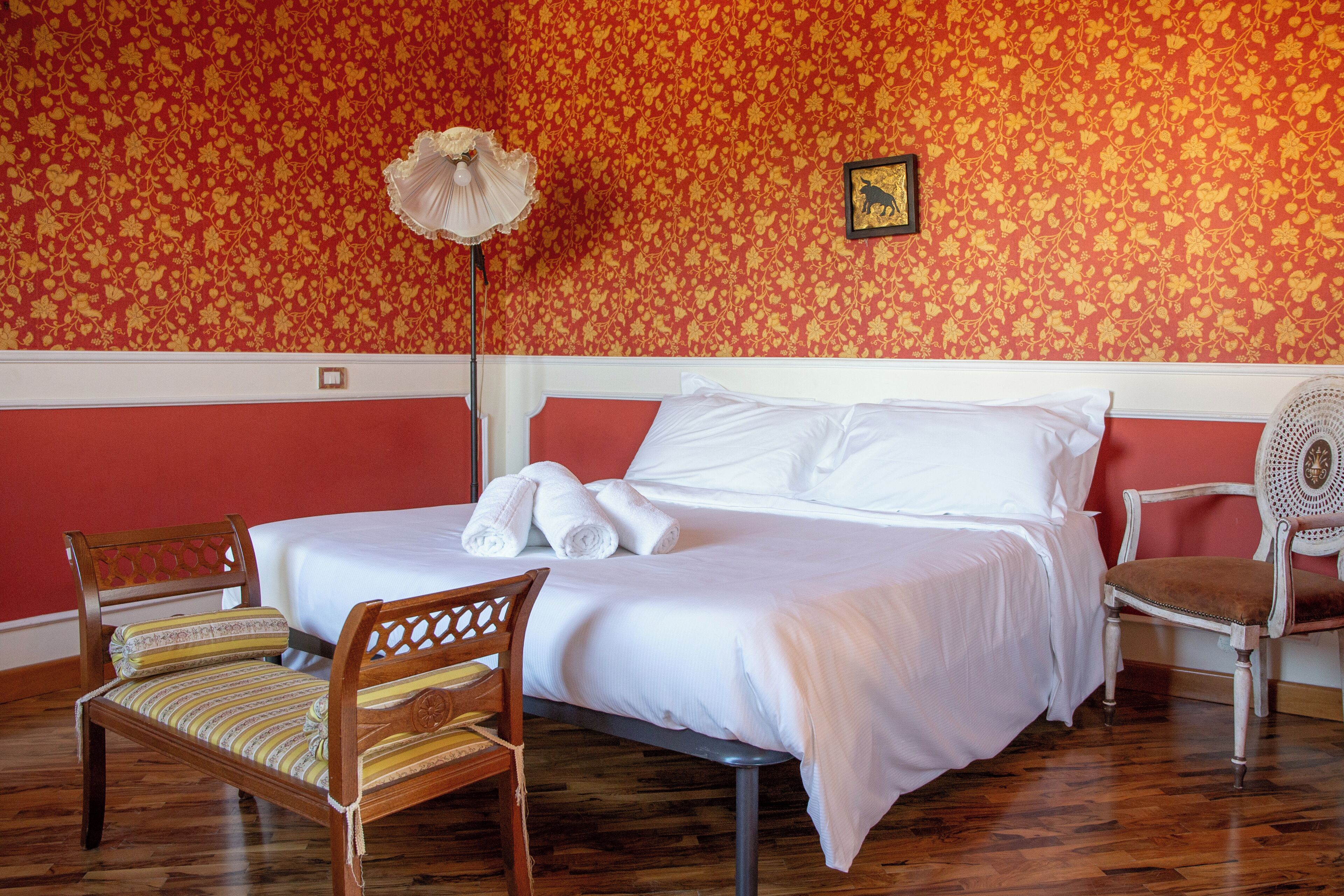 A hotel room with a bed, two chairs, a floor lamp, and a floral wallpaper.