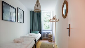 Ett sovrum med en säng, ett fönster, en hängande lampa och en spegel som är monterad på väggen.