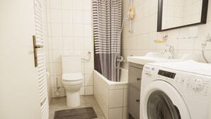 Ett litet badrum med toalett, badkar och en tvättmaskin med frontmatning.