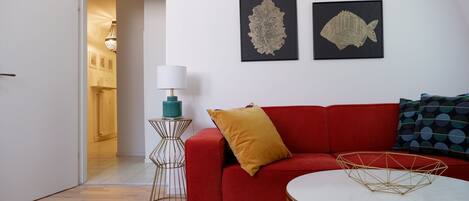 A modern living room with a red sofa, a white coffee table, and two framed fish art pieces on the wall.