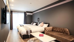 Quarto de hotel com uma cama grande, um sofá, uma mesinha e uma televisão fixada na parede.