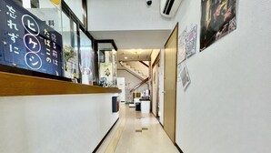 A hallway with a reception desk, a staircase, and a wall with various signs and posters. - Hotel Time Rich (Okinawa)