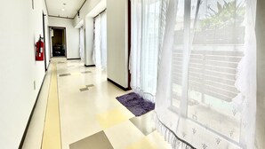 A hotel corridor with a fire extinguisher, a purple rug, and sheer curtains on large windows. - Hotel Time Rich (Okinawa)