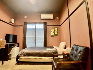 Un dormitorio con cama, televisor, una silla y una ventana con cortinas.