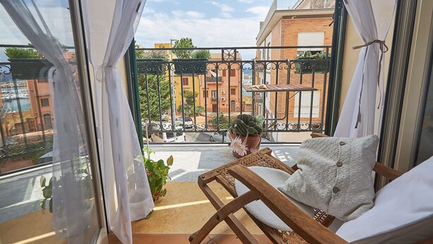 A balcony with a wooden chair, a potted plant, and a view of buildings. - Solemar Sicilia - Casa Olivia (Santa Flavia)