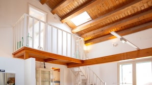 A spacious loft with exposed wooden beams, a glass cabinet, and a staircase leading to an upper level. - Solemar Sicilia - Casa Olivia (Santa Flavia)