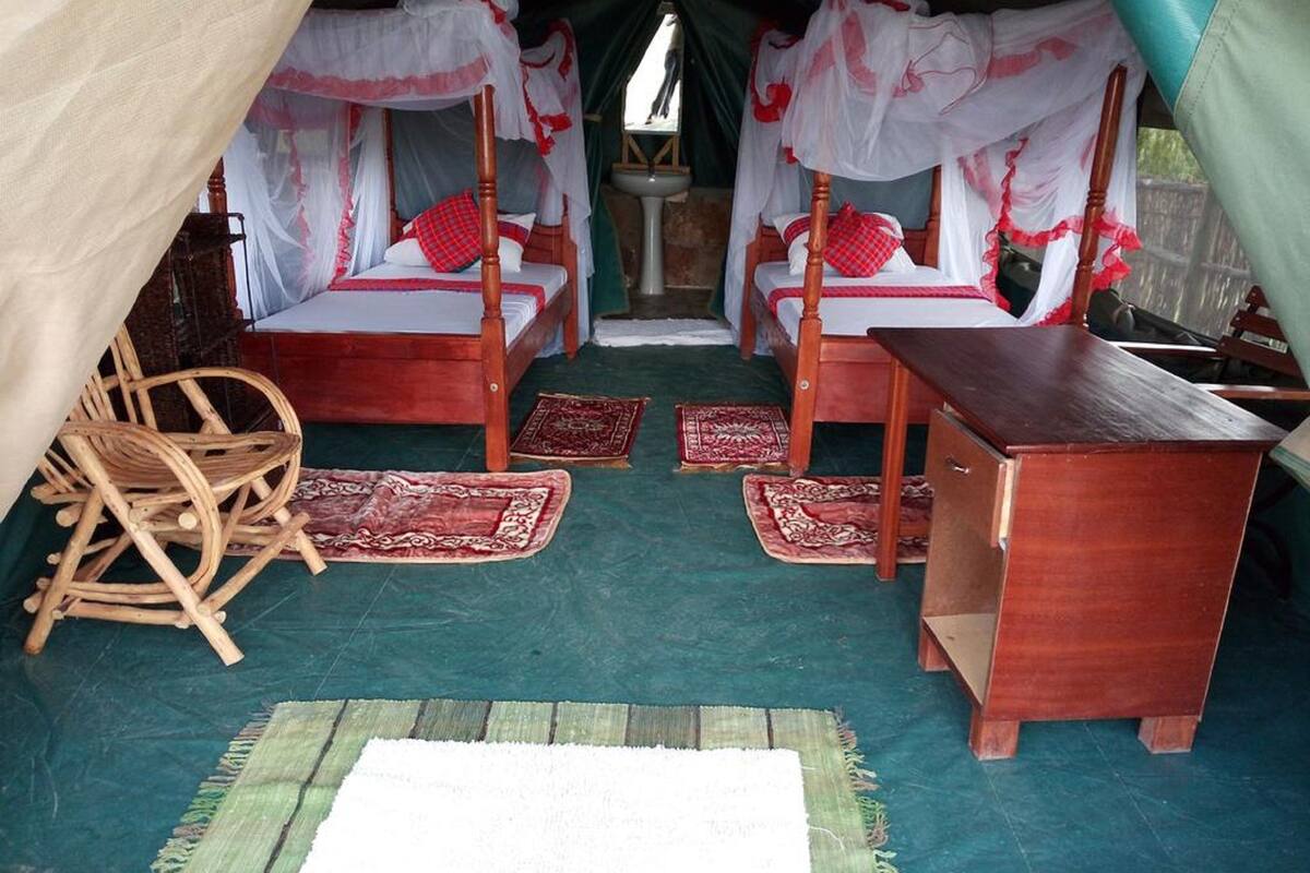 A tent-style room with two beds, a wooden bench, and a small table.