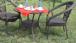A picnic setup with a table and two wicker chairs in a grassy field. - Mara Silalei (Narok)