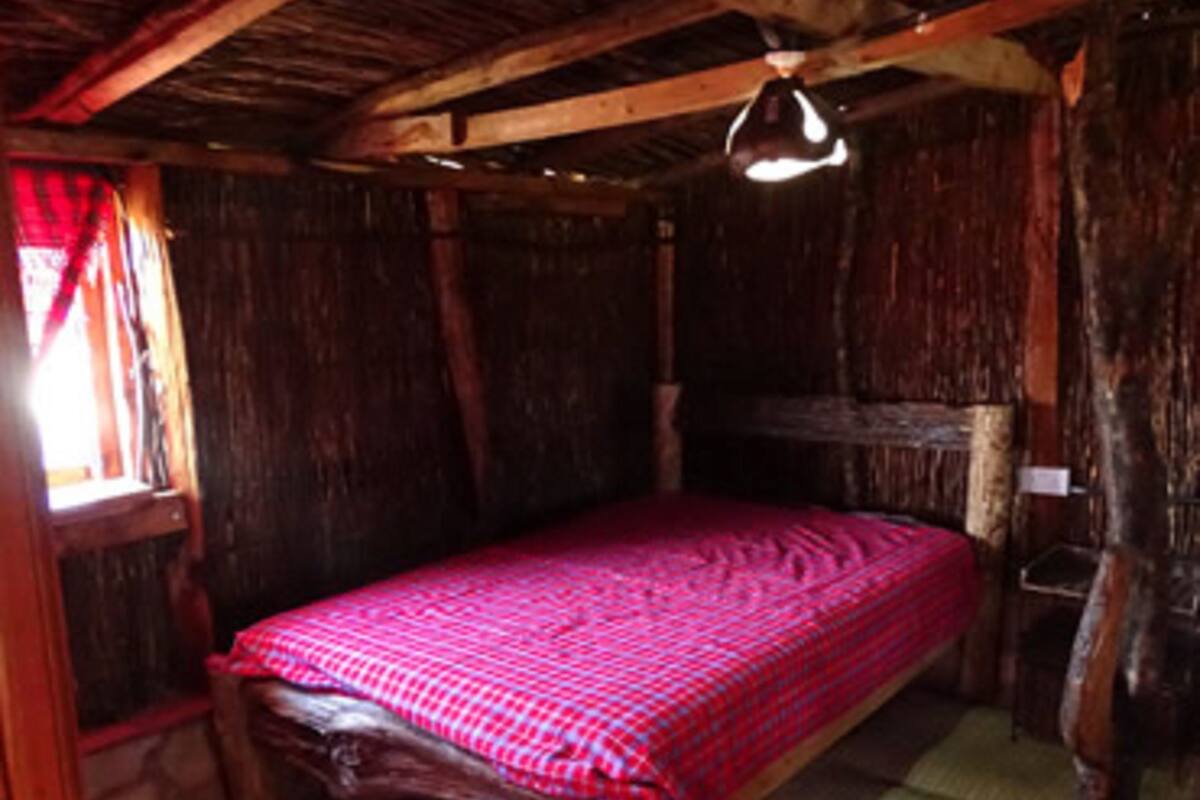 A rustic wooden room with a bed, a window with curtains, and a hanging light fixture.