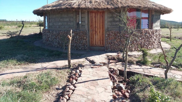 A small stone house with a thatched roof, a wooden door, and a small porch area. - Mara Silalei (Narok)