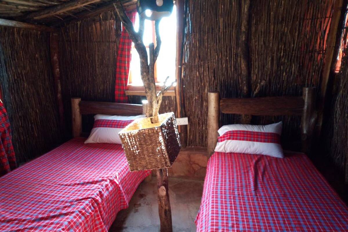 A rustic room with two beds, each with a red and white checkered bedspread, a wooden headboard, and a woven basket hanging from the ceiling.