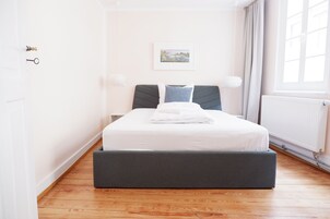 A bedroom with a bed, a window, a radiator, and a door.