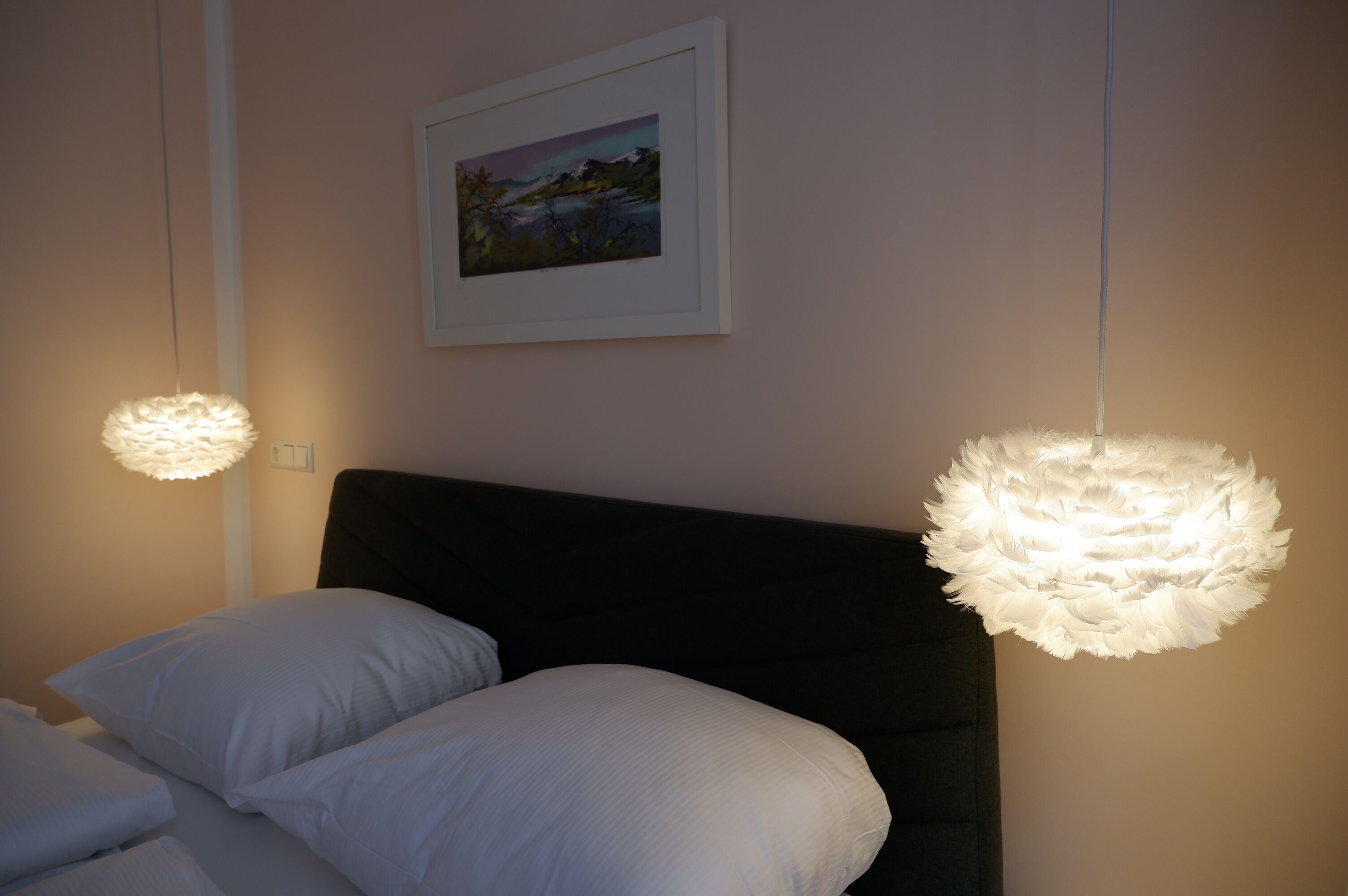 Ein Schlafzimmer mit einem Bett, zwei weißen Kissen, einem gerahmten Bild an der Wand und zwei Pendelleuchten.