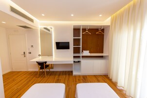 Una habitación de hotel moderna con piso de madera, un escritorio con silla, un televisor montado en la pared, un armario con espacio para colgar y dos camas.