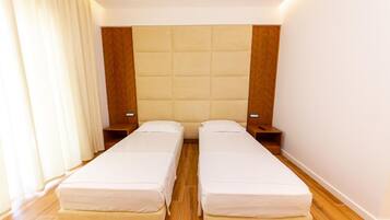 Habitación doble con dos camas individuales, cabecero de madera, mesitas de noche y un ventanal con cortinas.
